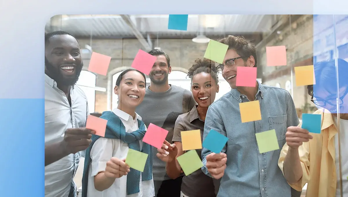 Creative team smiling in front of glass wall covered with sticky notes