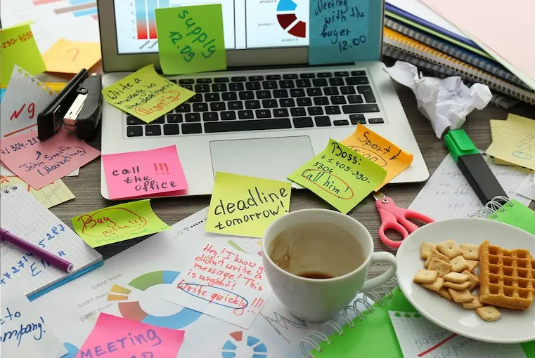 Desk with laptop full of sticky notes, waffles and empty cup of a coffee